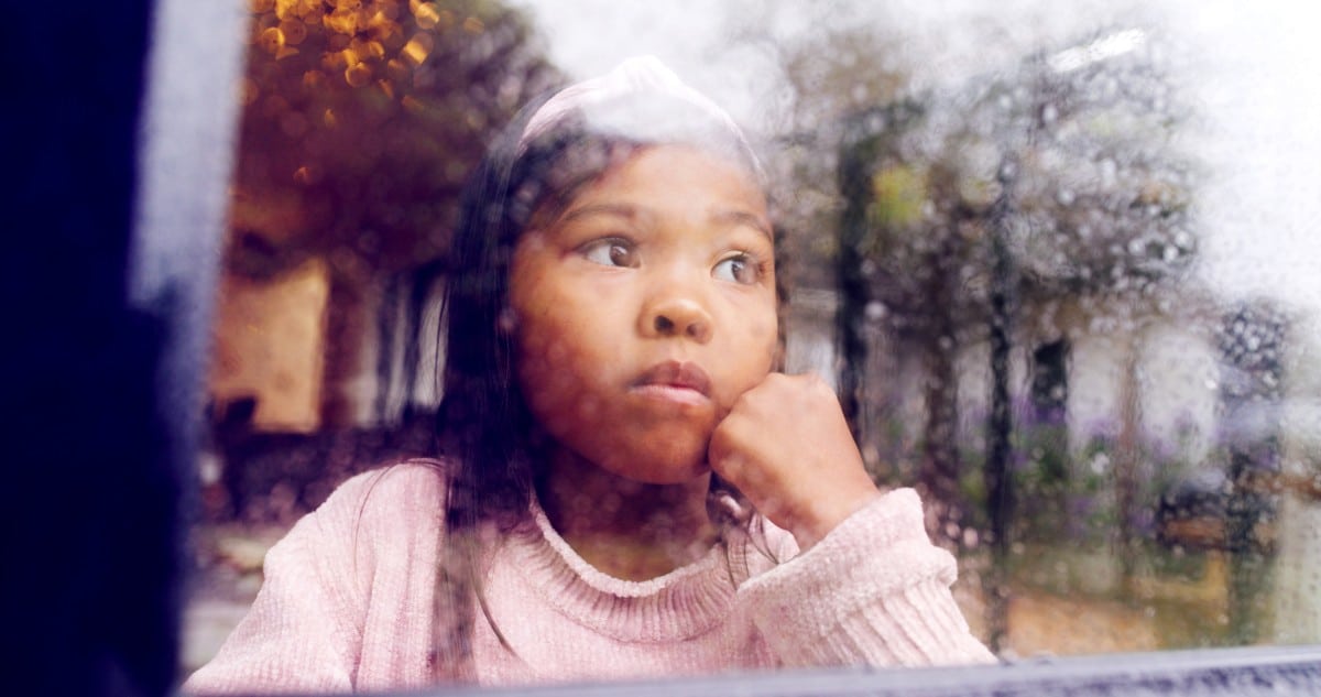 child sitting by the window watching the rain